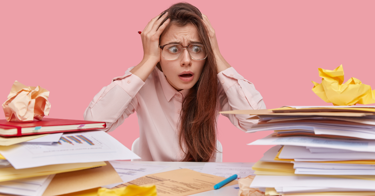 An overwhelmed student looks at a pile of papers and books.