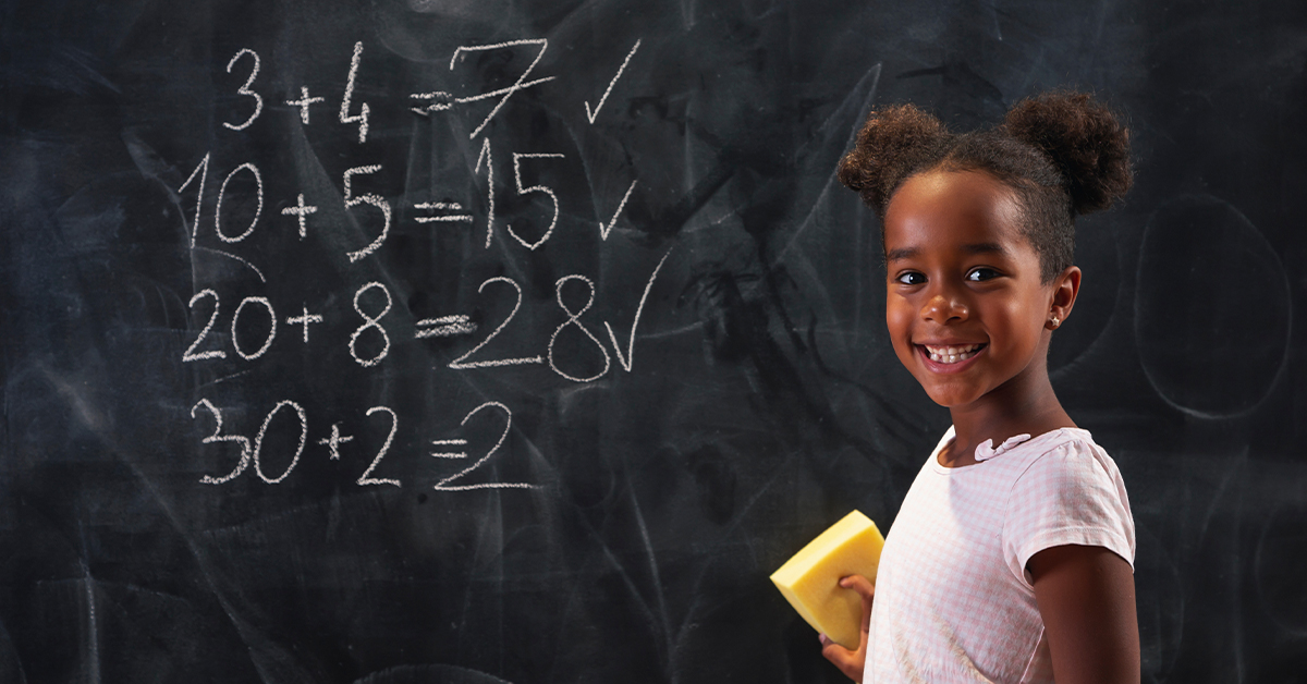 A young girl doing addition facts on a chalkboard.