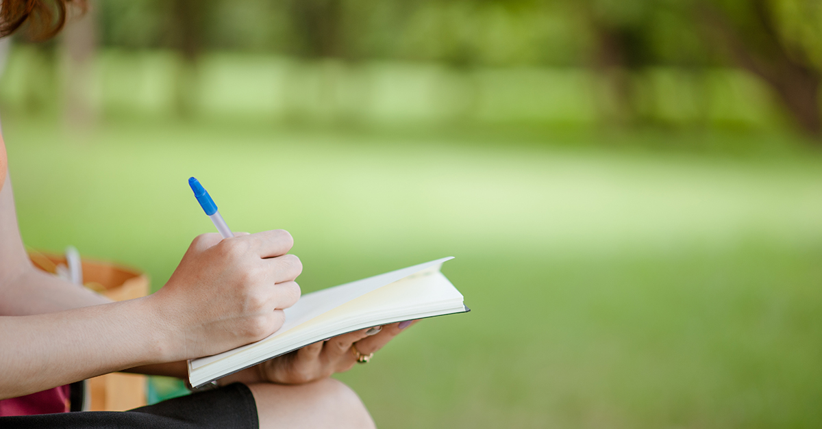 A person sitting outside while writing in a journal.