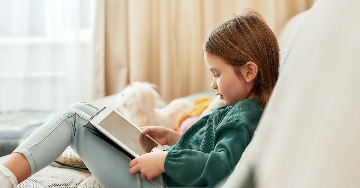 Young girl in a green sweater sits on the couch while using an app on her tablet.