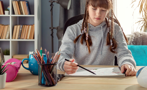 Teenaged girl drawing on paper on a desk at home.