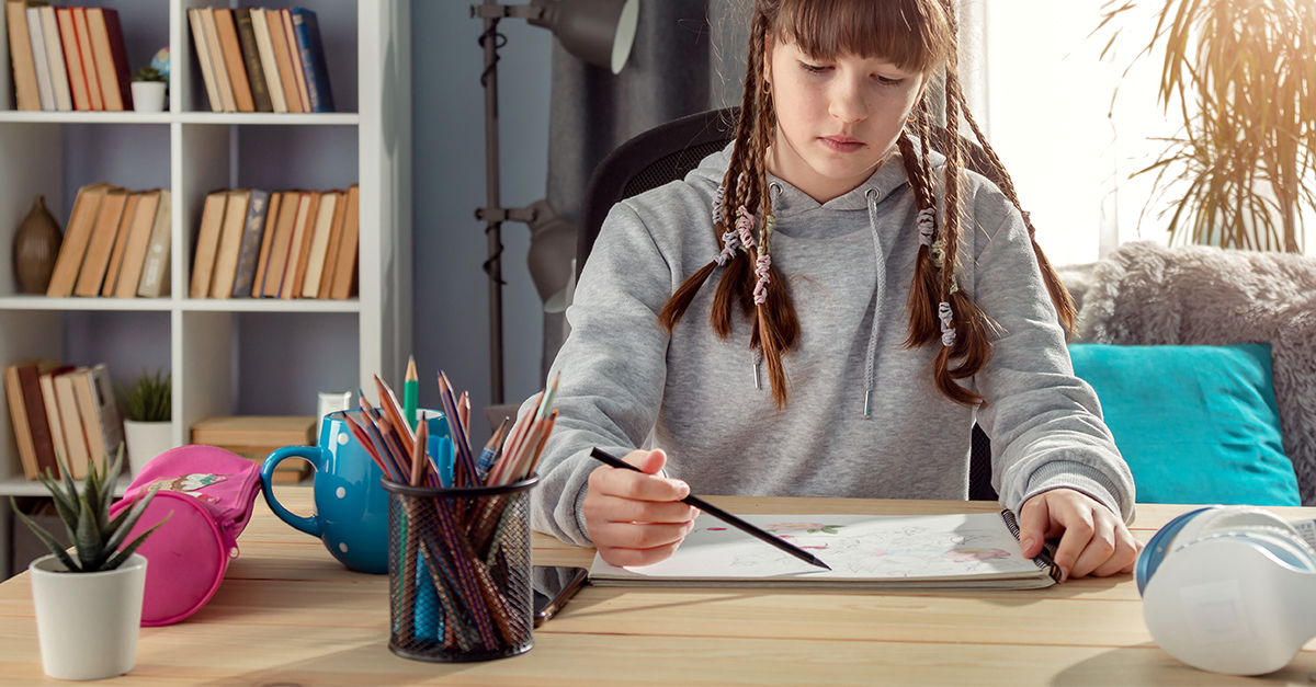 Teenaged girl drawing on paper on a desk at home.