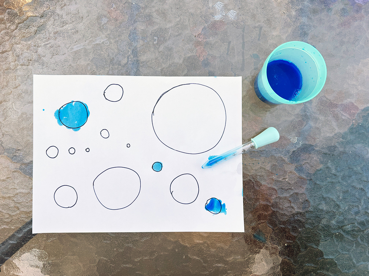 A piece of paper, an eyedropper, and a cup of blue dyed water.