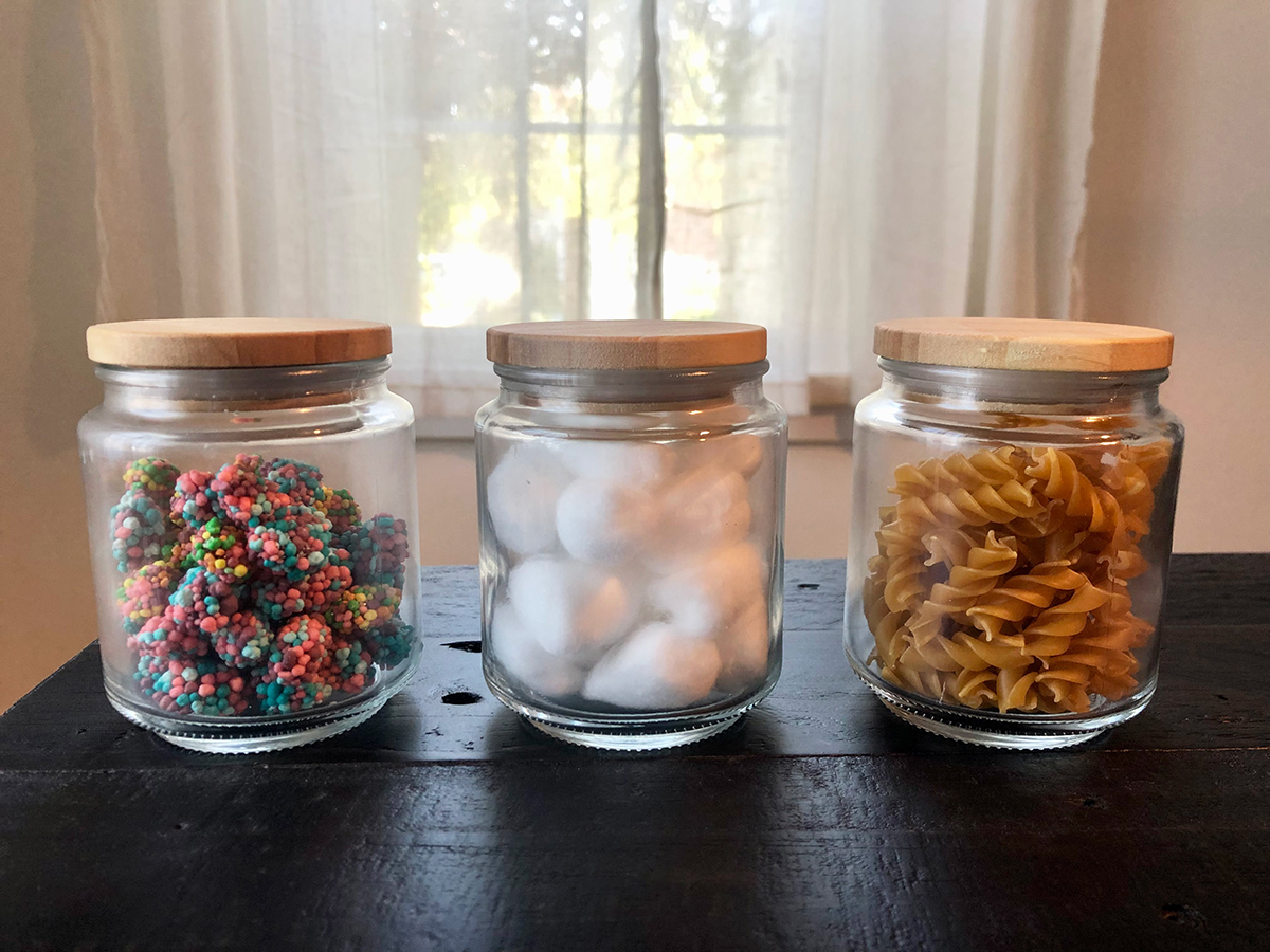 Three small jars filled with candies, cotton balls, and pasta noodles.