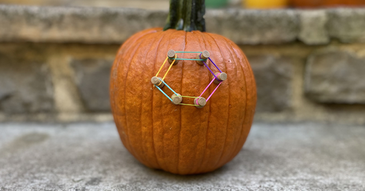A pumpkin with push pins connected by rubber bands in the shape of a hexagon.