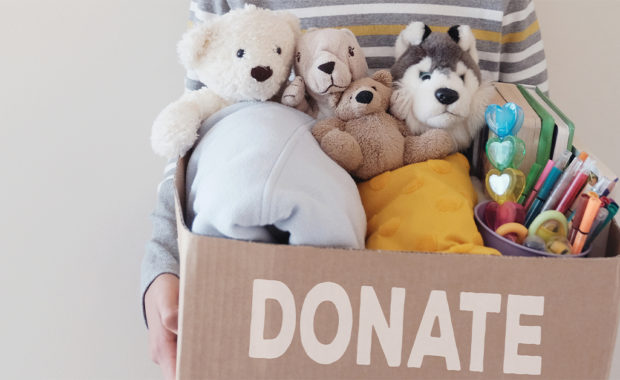 Little boy holding a cardboard box full of toys and craft supplies to donate.