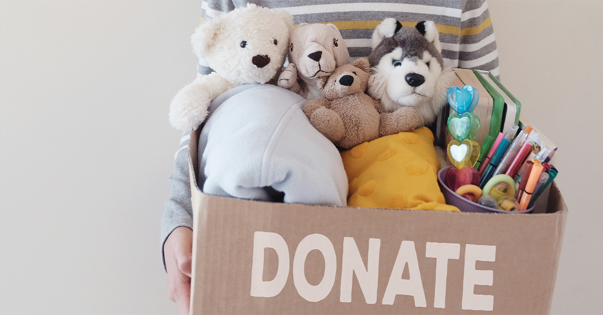 Little boy holding a cardboard box full of toys and craft supplies to donate.