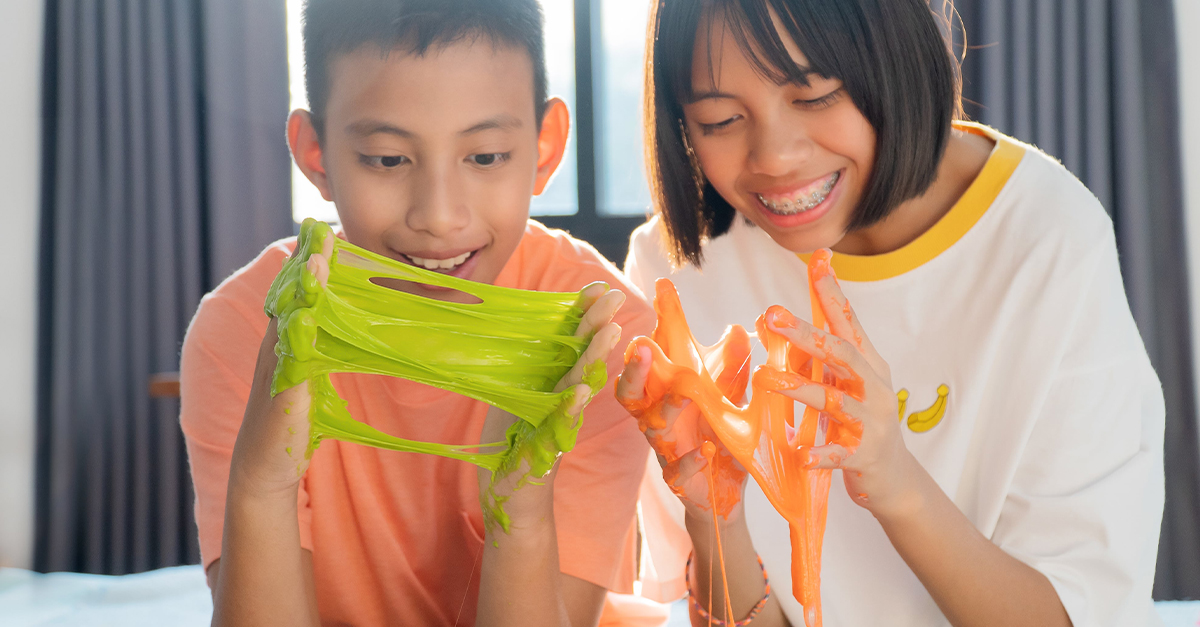 Two preteens stretch gooey, green and orange slime between their hands.