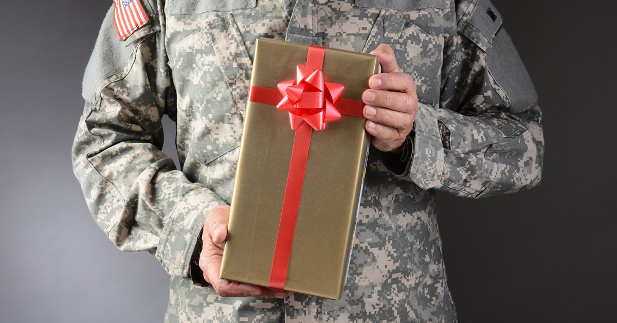 American soldier holding a gold-wrapped gift with a red ribbon and bow.