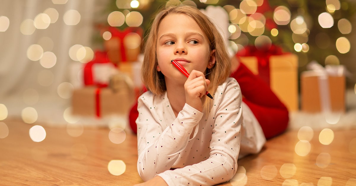 Young girl laying on the floor near Christmas tree with a pencil and paper.