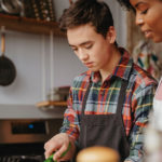 A teenage boy helps cut vegetables for a meal.