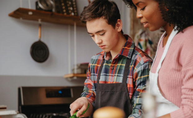 A teenage boy helps cut vegetables for a meal.