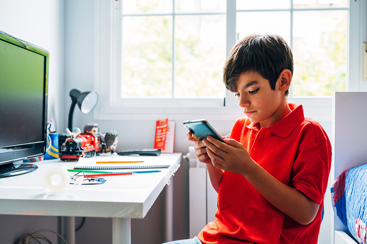 Preteen boy uses a smartphone while sitting at his desk.