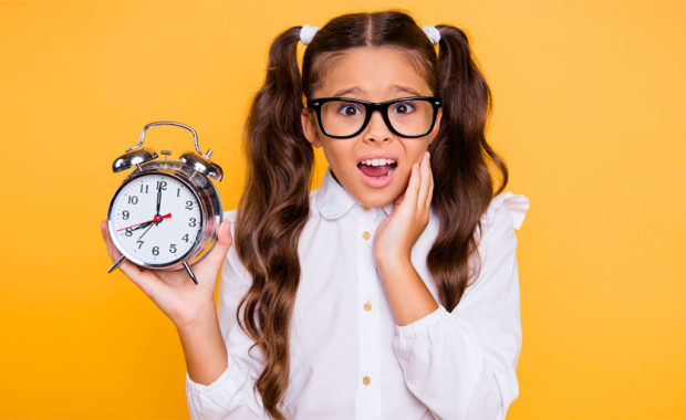 Young girl looks worried while holding up a clock.