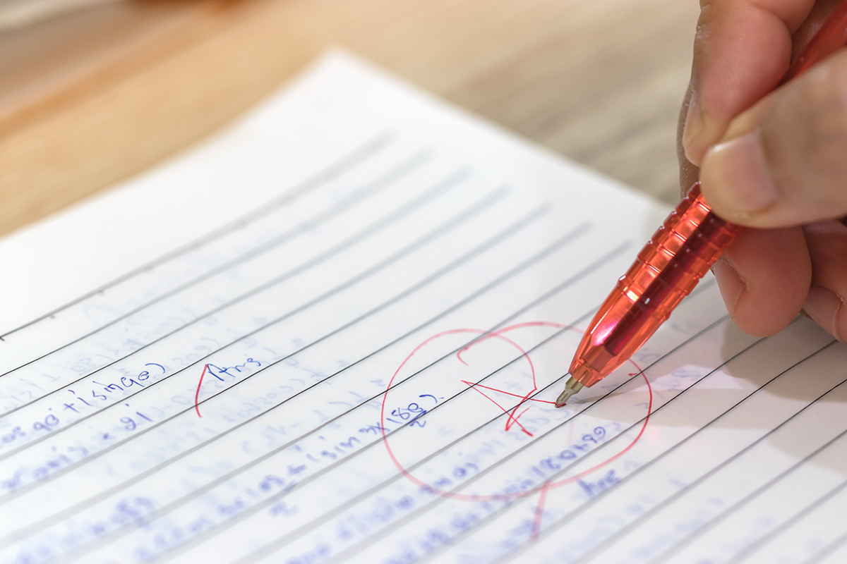 A teacher puts an A on an assignment with a red pen.