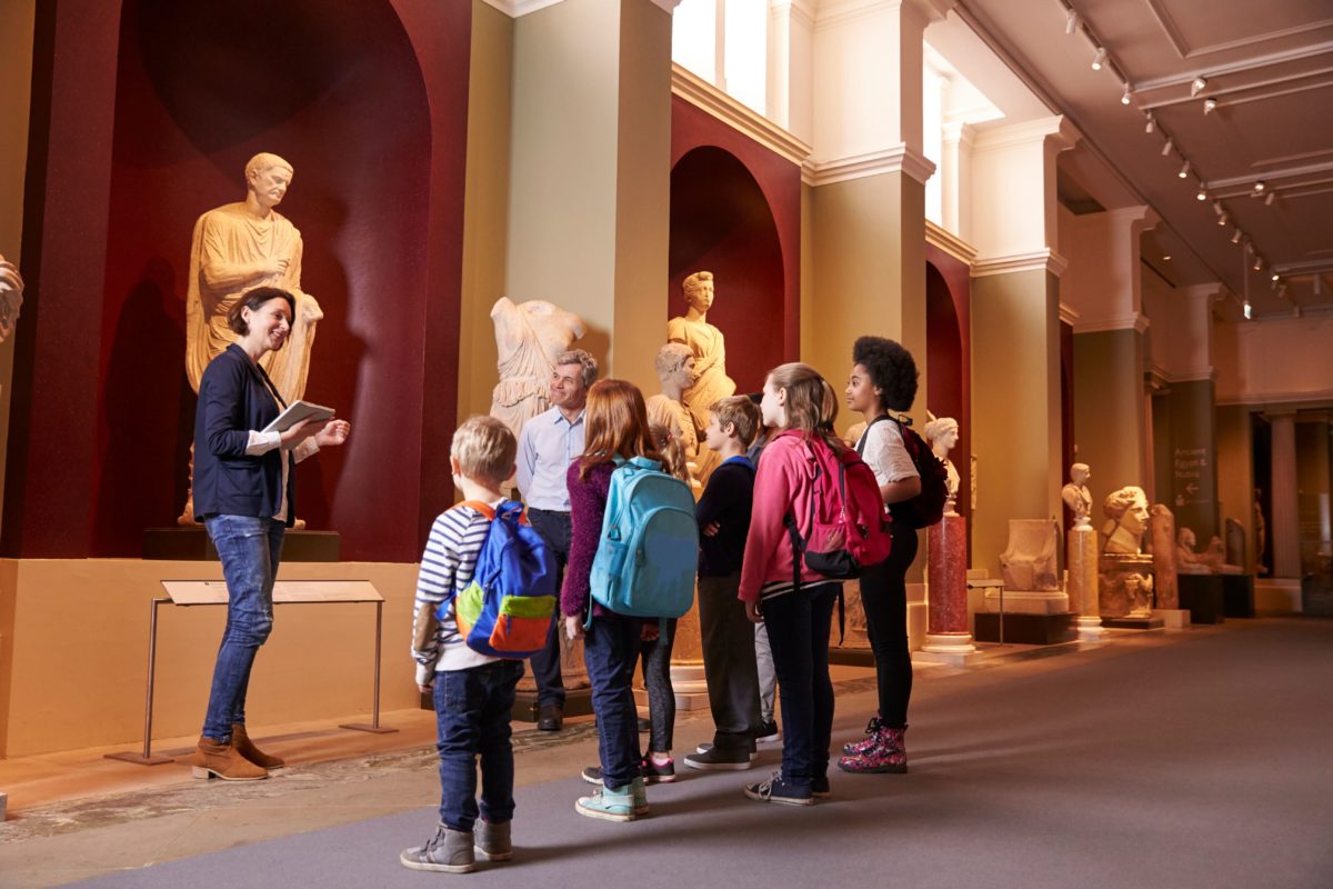 A group of students and their teacher view historic sculptures at a museum.