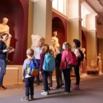 A group of students and their teacher view historic sculptures at a museum.