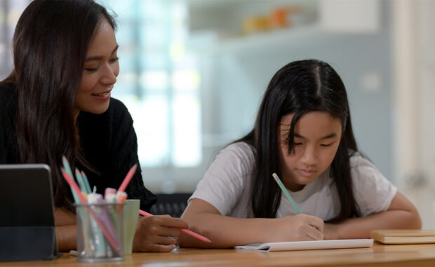 Mom helps daughter as she completes schoolwork.