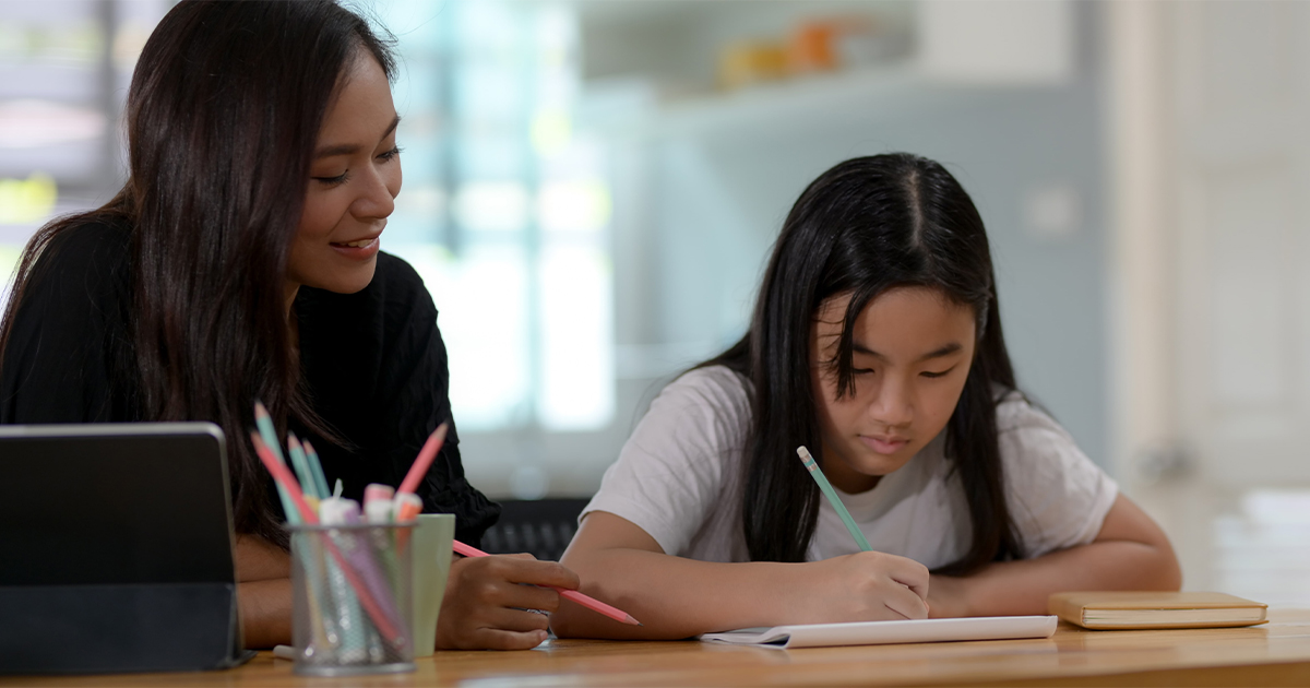 Mom helps daughter as she completes schoolwork.