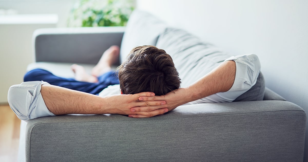 A man relaxes on a gray couch.