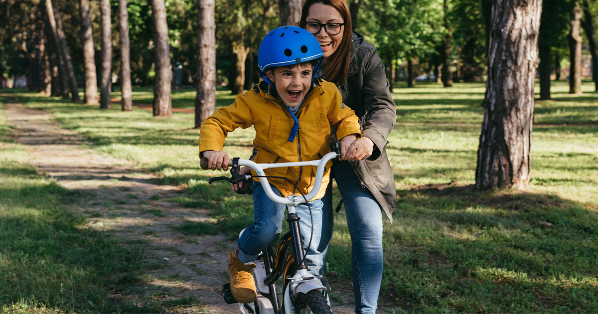 Young woman holds up little boy while he learns how to ride a bike.