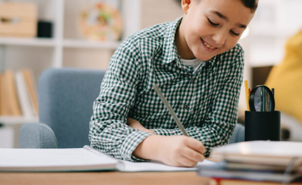 Young boy smiles as while doing schoolwork.