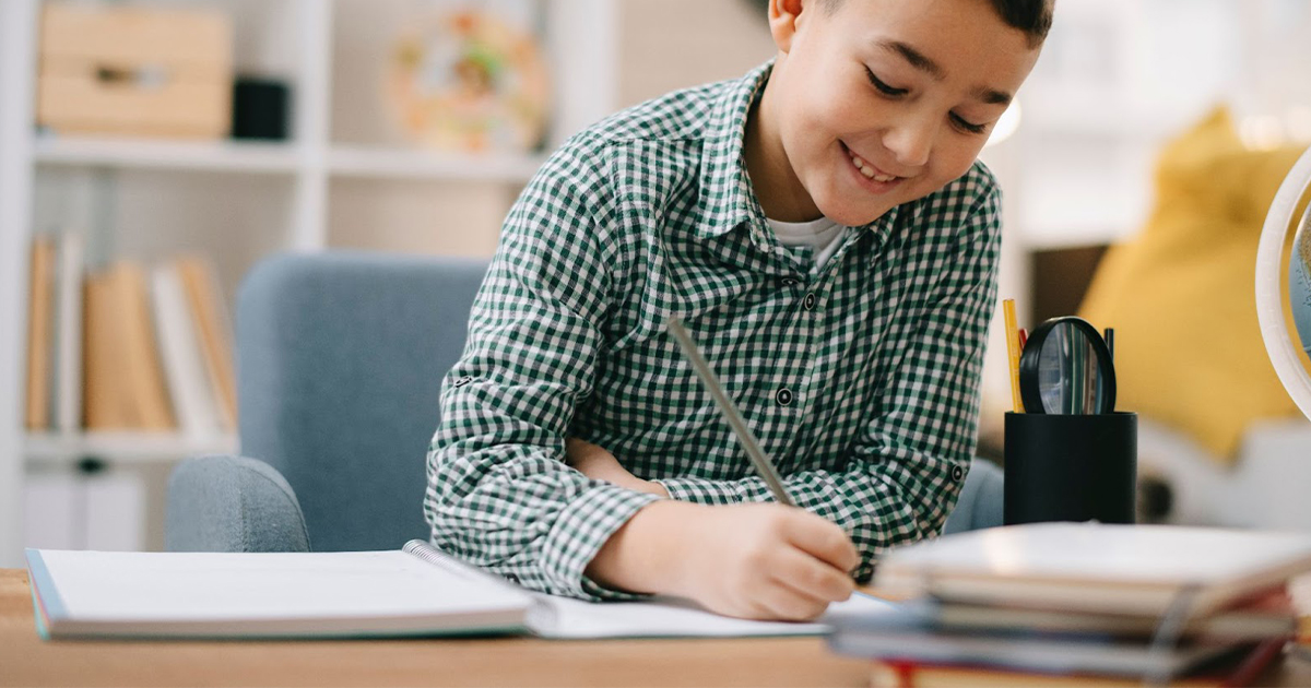 Young boy smiles as while doing schoolwork.