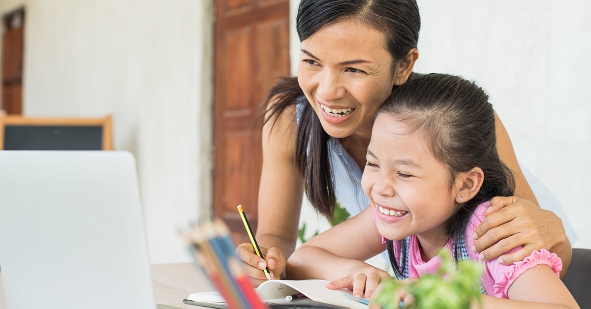 A mother and daughter smile while working on a laptop.