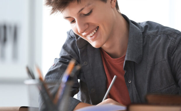 Teenage boy smiles while doing schoolwork.