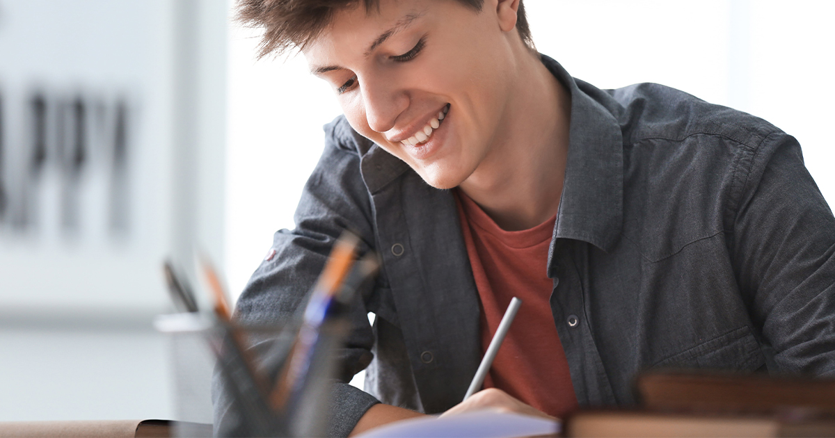 Teenage boy smiles while doing schoolwork.