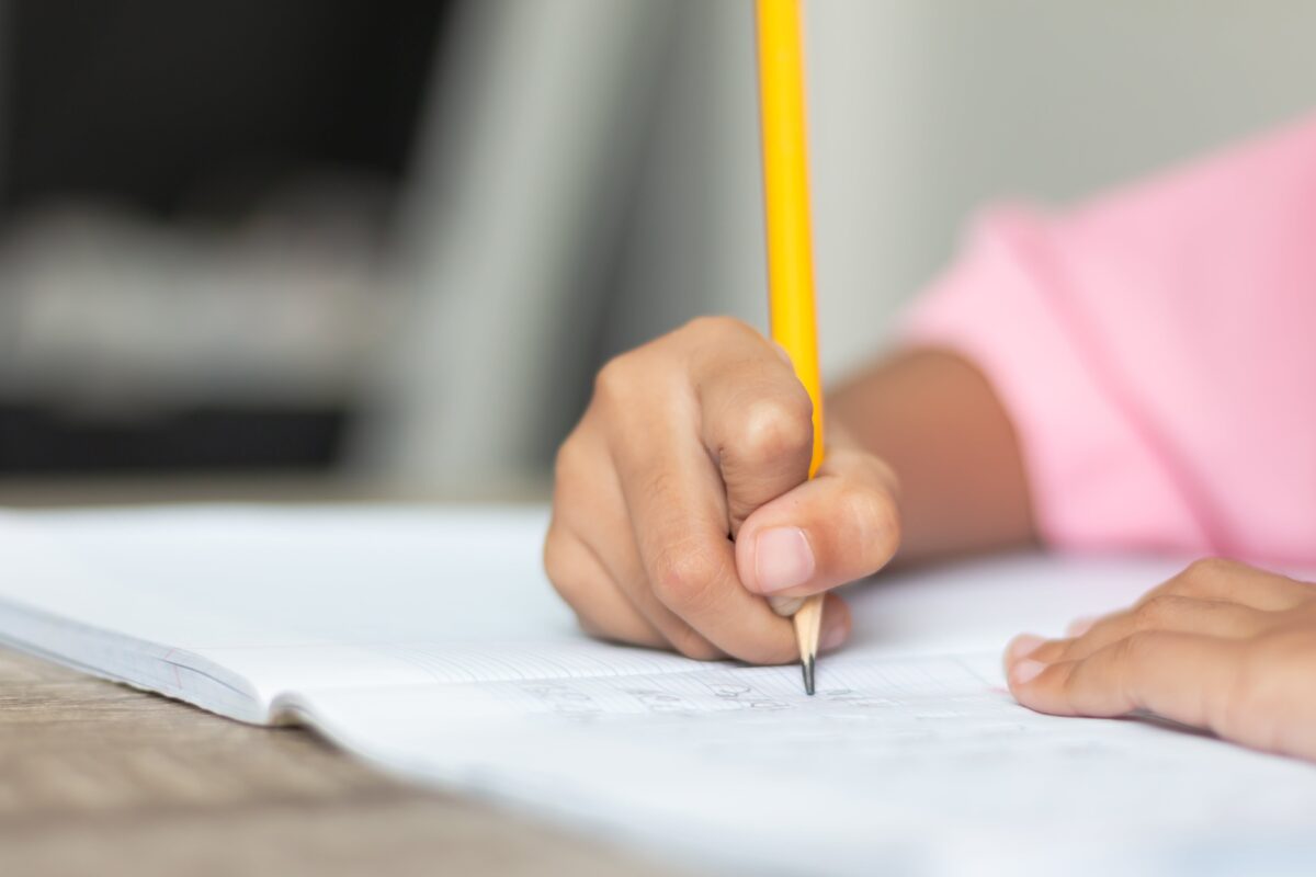 A hand grips a yellow pencil while writing in a composition book.