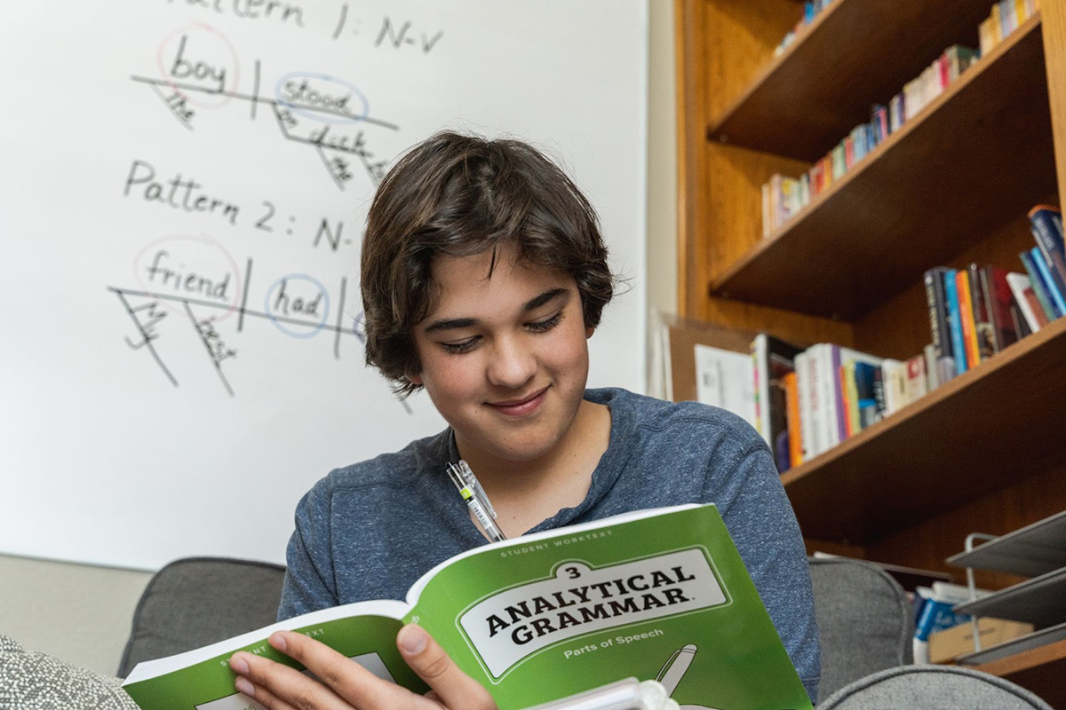 A boy smiles while working in his Analytical Grammar workbook.