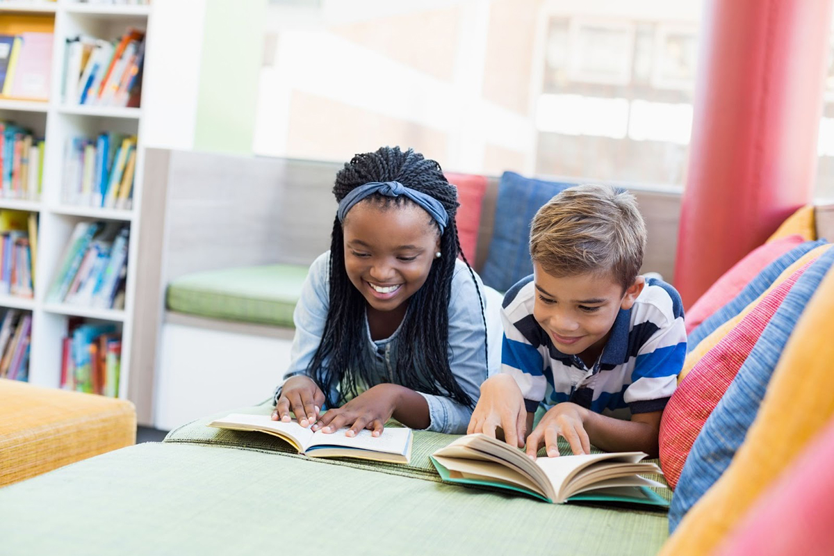 A young male and female student read independently on a green couch.