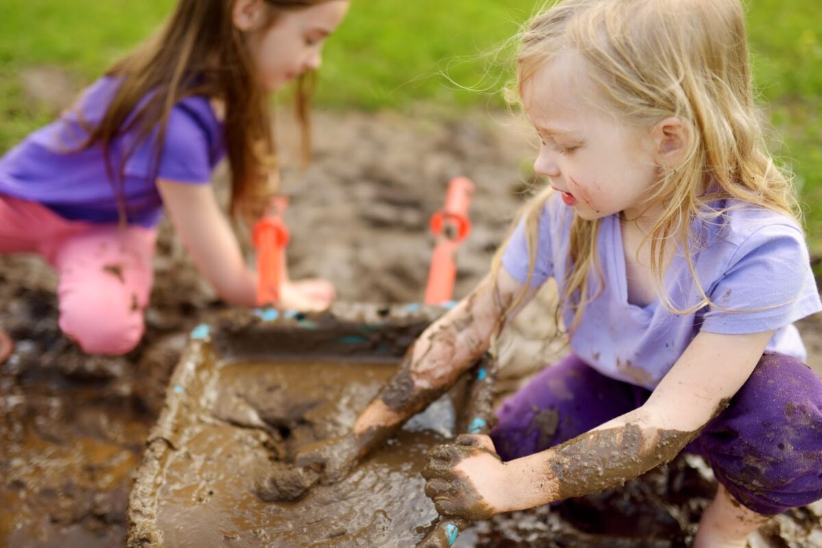 Two young girls play in the mud outside.