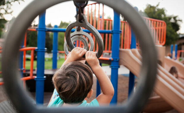 A young child plays on the monkey bars at a playground.