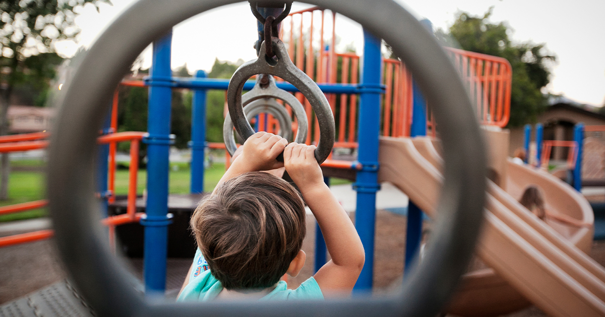 A young child plays on the monkey bars at a playground.