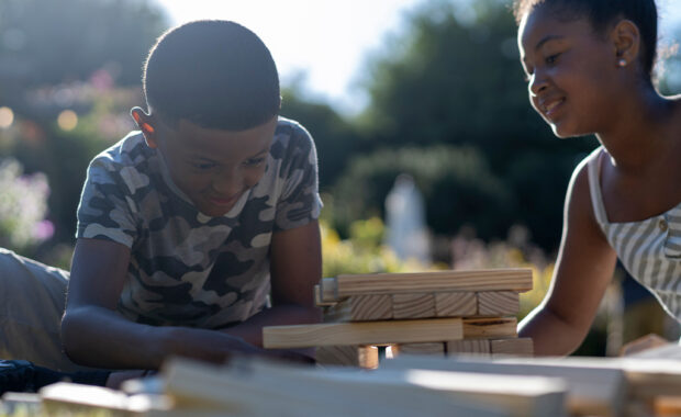 A brother and sister play with blocks outside.