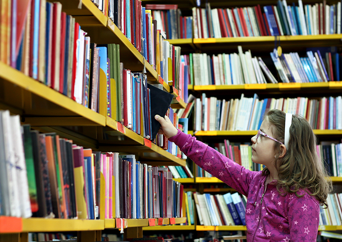 A young girl picks a book off the shelf at the library