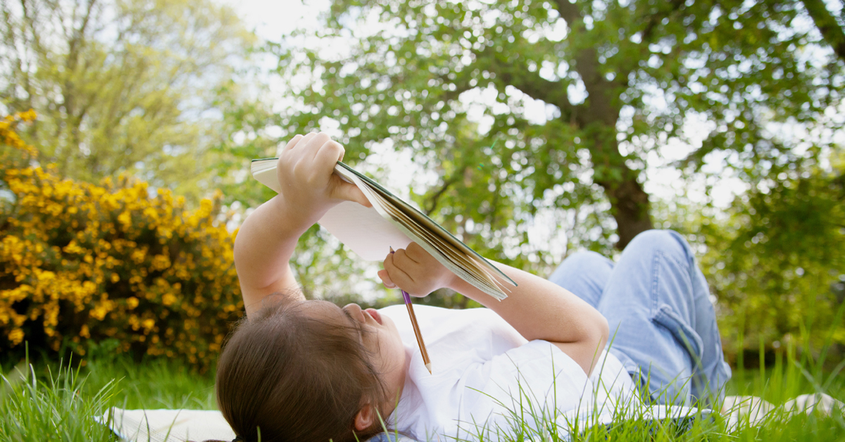 A young girl writes outside.