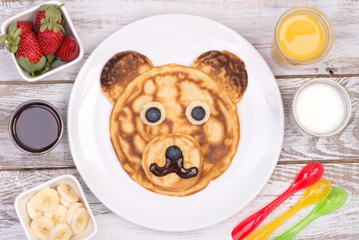 Breakfast pancakes in the shape of a bear with fruits and toppings.