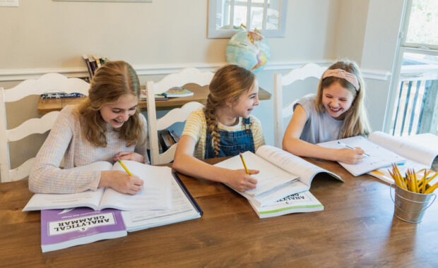 Three young girls smile while working in a grammar booklet.