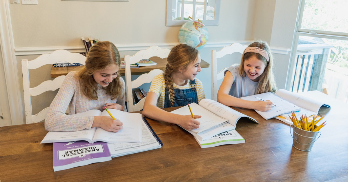Three young girls smile while working in a grammar booklet.