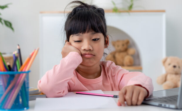 A bored child sits at a table staring at their homework.