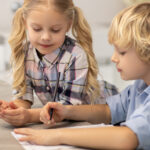 A young girl and boy write side-by-side.