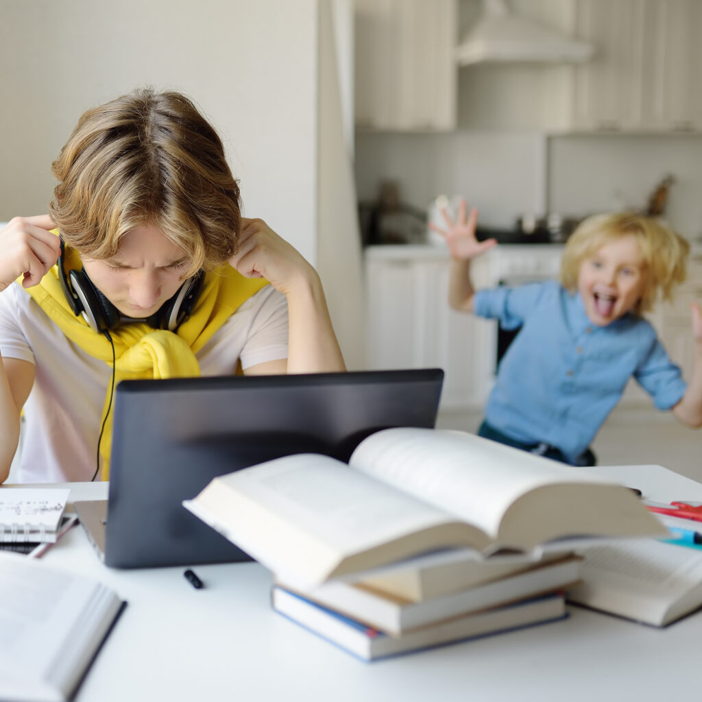 A young student doing homework with distractions in the background.