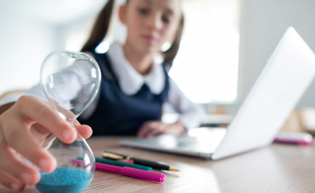 A young student looks at an hourglass while doing homework.