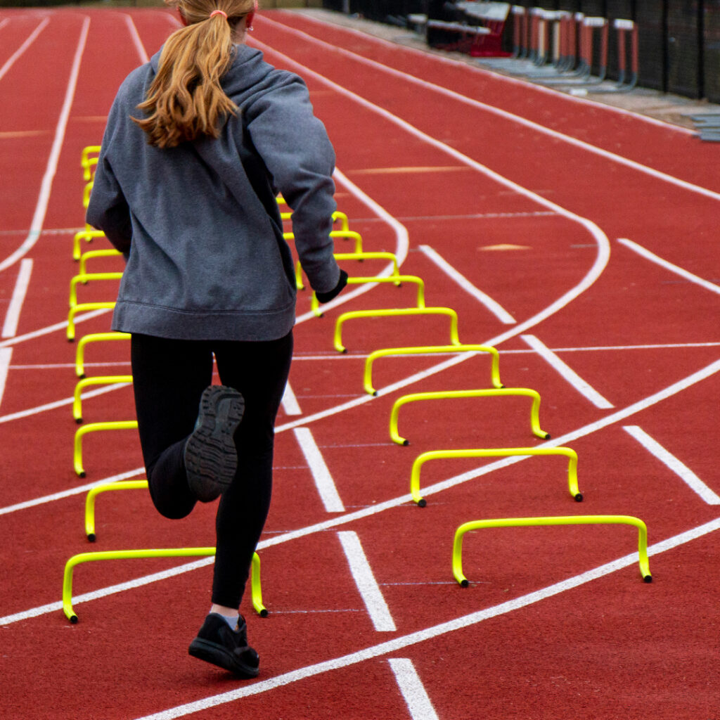 Teenage running on a track over hurdles.