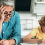 A child writing with a parent sitting next to them.