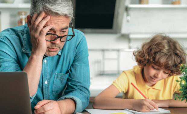 A child writing with a parent sitting next to them.