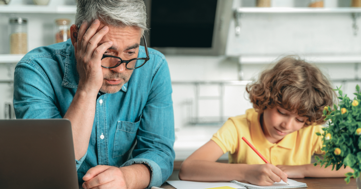 A child writing with a parent sitting next to them.